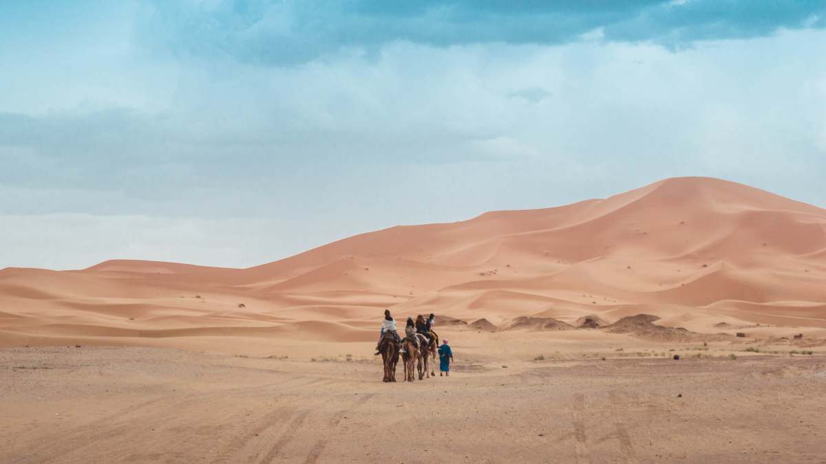 desert person riding on camel across the desert sand